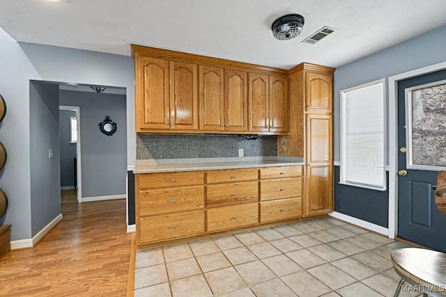 kitchen featuring visible vents, baseboards, light countertops, decorative backsplash, and brown cabinets