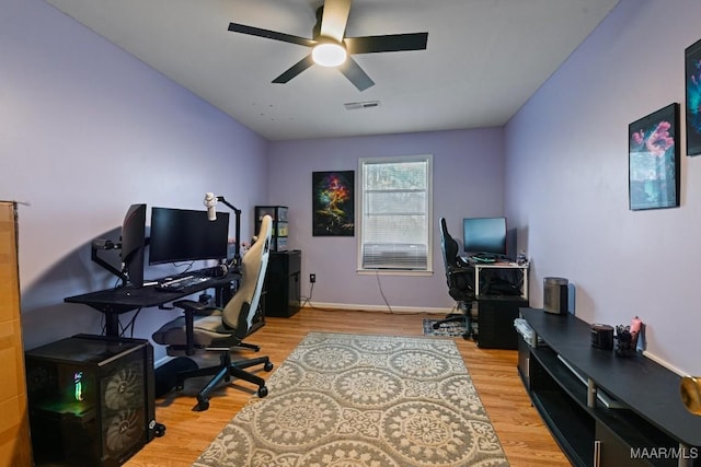 office space with baseboards, light wood-type flooring, visible vents, and a ceiling fan