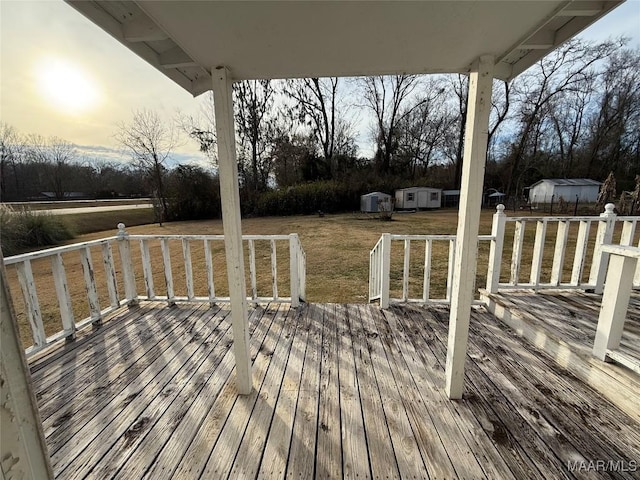 deck at dusk featuring a storage shed and a lawn