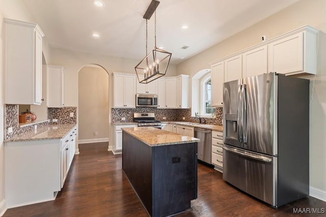 kitchen featuring light stone counters, a center island, decorative backsplash, arched walkways, and appliances with stainless steel finishes
