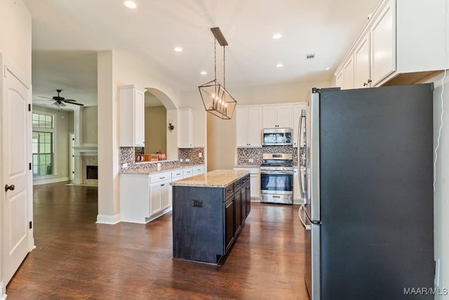 kitchen featuring light stone counters, a center island, hanging light fixtures, stainless steel appliances, and white cabinets