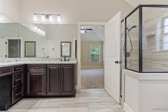 full bath featuring ceiling fan, tiled shower, vaulted ceiling, a sink, and double vanity