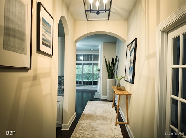 hallway with arched walkways, a notable chandelier, baseboards, and dark wood finished floors