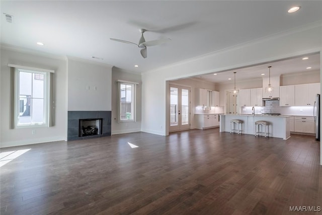 unfurnished living room featuring ceiling fan, ornamental molding, dark hardwood / wood-style flooring, and a tile fireplace