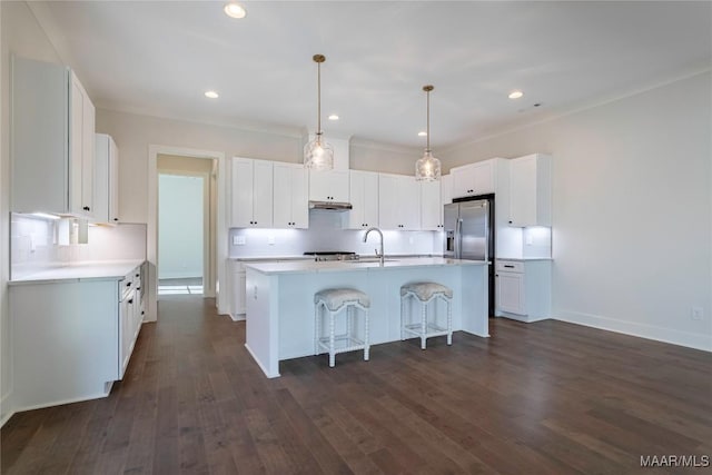 kitchen featuring white cabinetry, a center island with sink, stainless steel fridge, and a kitchen breakfast bar