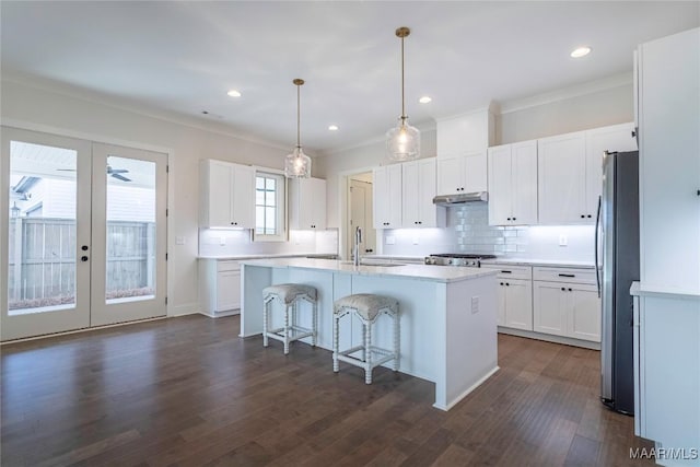 kitchen with a breakfast bar, pendant lighting, white cabinetry, stainless steel fridge, and a kitchen island with sink