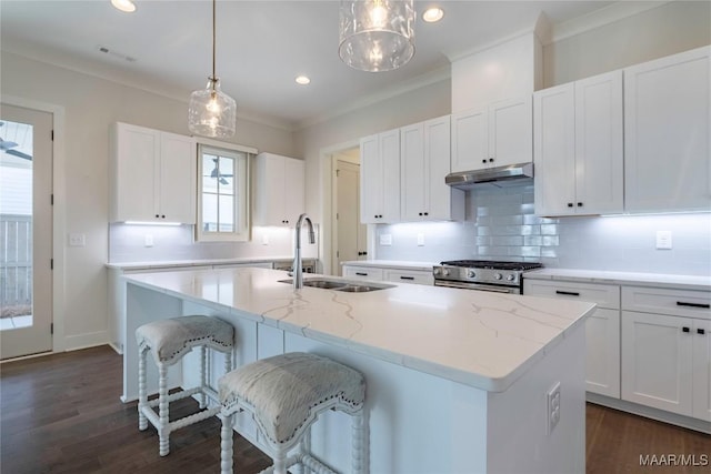 kitchen featuring decorative light fixtures, an island with sink, sink, white cabinets, and light stone counters