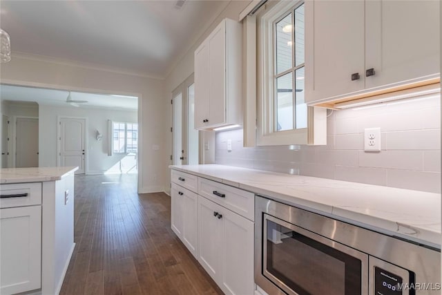 kitchen with tasteful backsplash, stainless steel microwave, white cabinets, and light stone counters