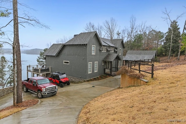 view of property exterior with driveway, roof with shingles, a water view, and an outdoor structure