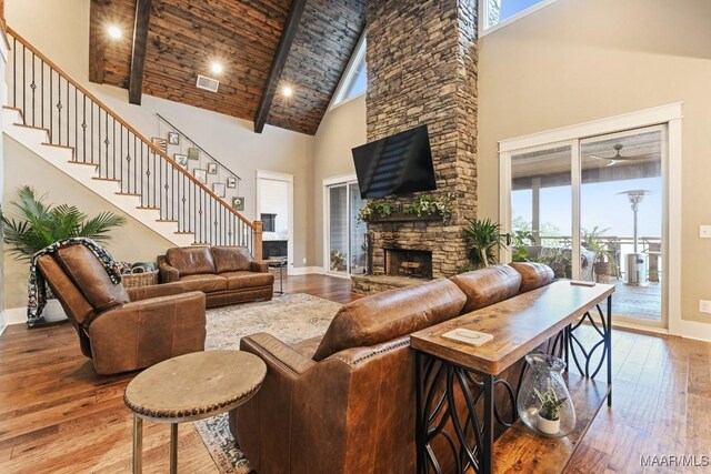 living room featuring a stone fireplace, wood ceiling, high vaulted ceiling, beam ceiling, and hardwood / wood-style floors