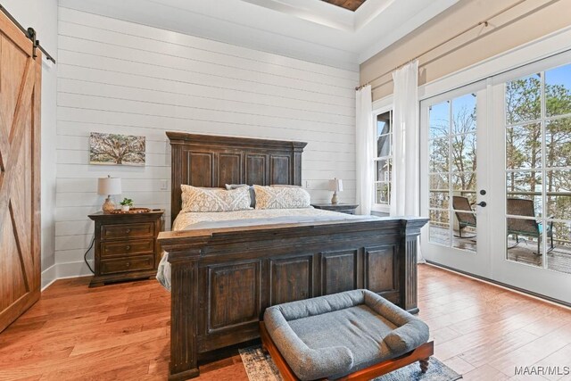 bedroom featuring light hardwood / wood-style floors, a barn door, access to outside, french doors, and wood walls