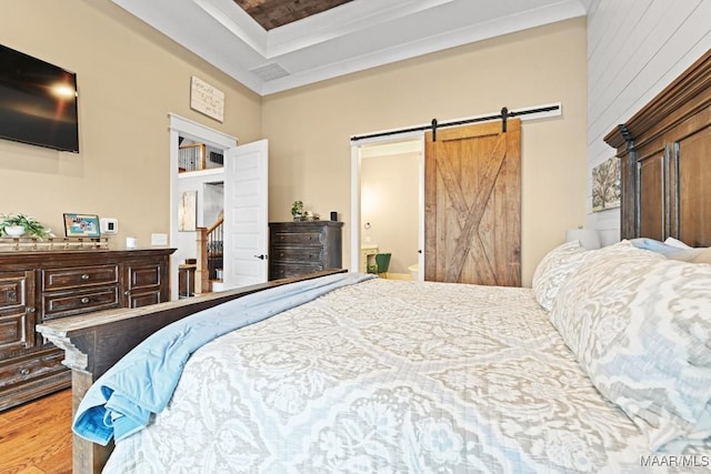 bedroom with ensuite bathroom, a barn door, a tray ceiling, and light hardwood / wood-style flooring