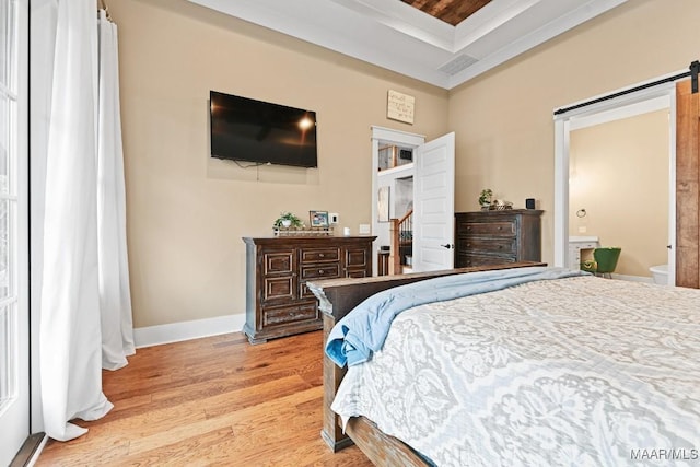 bedroom featuring a tray ceiling, a barn door, and light hardwood / wood-style flooring