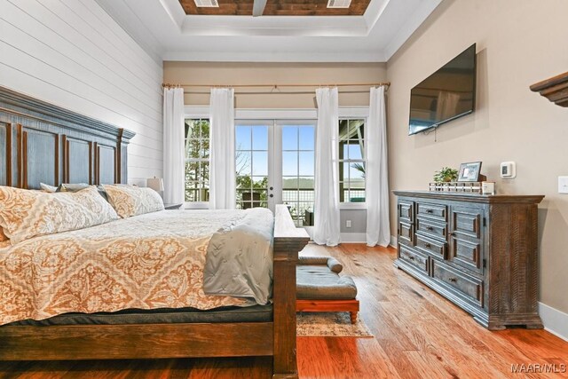 bedroom featuring access to exterior, a tray ceiling, french doors, and light wood-type flooring