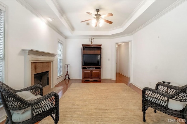 living room featuring light hardwood / wood-style flooring, ceiling fan, a high end fireplace, ornamental molding, and a raised ceiling