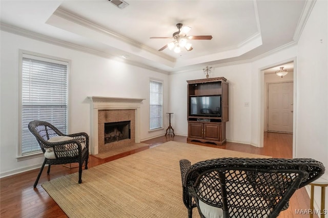 living room with crown molding, wood-type flooring, a tray ceiling, ceiling fan, and a high end fireplace