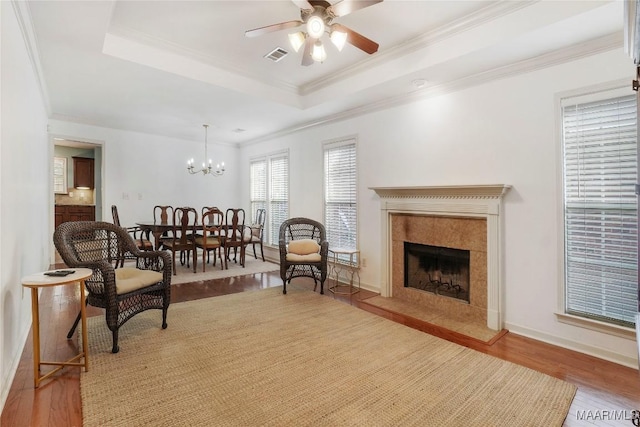 living area with hardwood / wood-style flooring, crown molding, ceiling fan with notable chandelier, and a tray ceiling