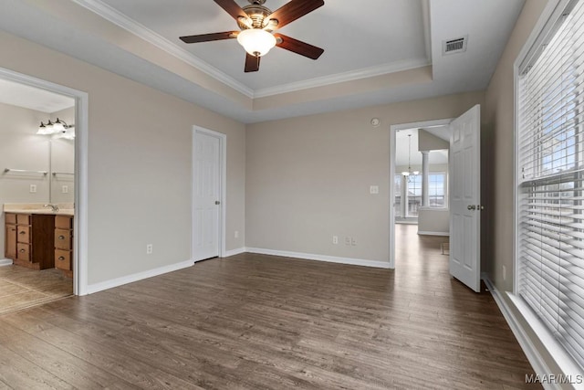 unfurnished bedroom featuring ornamental molding, dark wood-type flooring, ensuite bathroom, and a tray ceiling