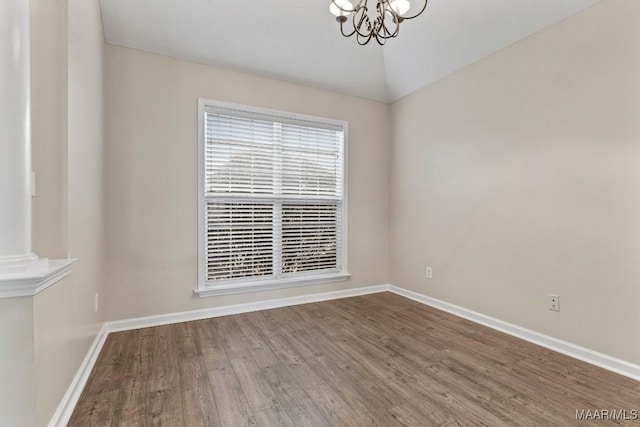 spare room featuring vaulted ceiling, hardwood / wood-style floors, and a notable chandelier