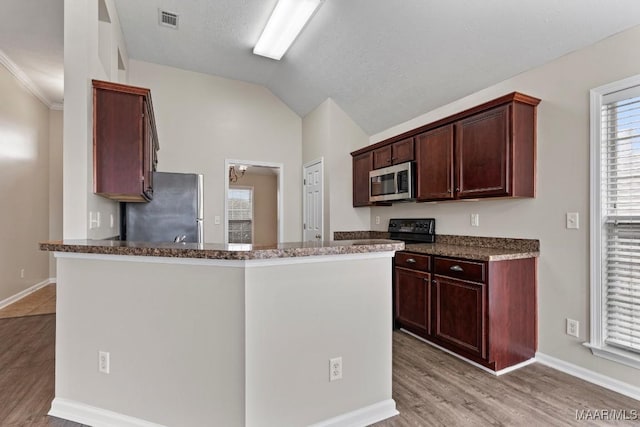 kitchen with lofted ceiling, a textured ceiling, light wood-type flooring, appliances with stainless steel finishes, and dark stone counters