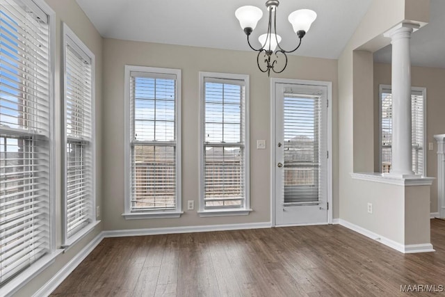 unfurnished dining area featuring dark wood-type flooring, decorative columns, and a notable chandelier