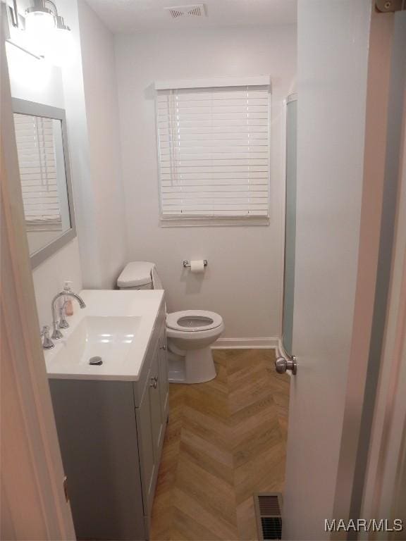 bathroom with parquet floors, vanity, toilet, and a shower with door