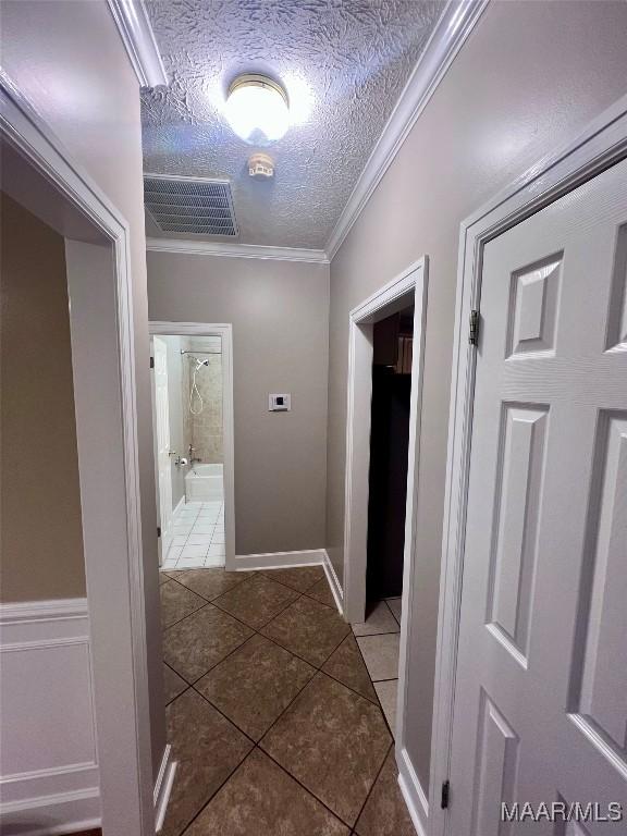 hallway with crown molding, dark tile patterned flooring, and a textured ceiling