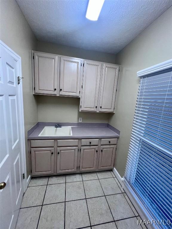 clothes washing area with sink, light tile patterned floors, and a textured ceiling