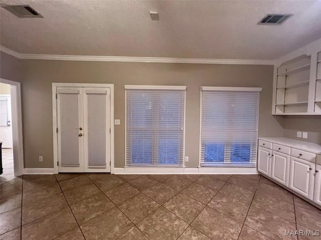 unfurnished dining area with dark tile patterned floors, ornamental molding, french doors, and a textured ceiling