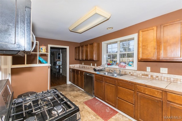 kitchen with sink, tile counters, stainless steel gas range, and dishwasher