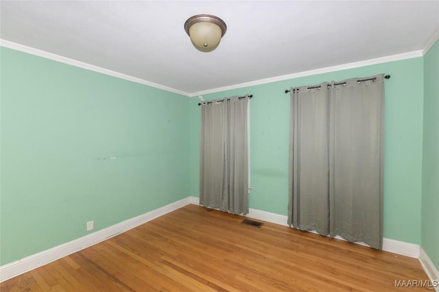 empty room with ornamental molding, visible vents, baseboards, and wood finished floors