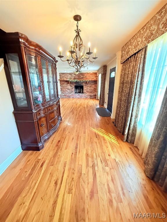 dining space with an inviting chandelier, light wood-style flooring, a fireplace, and baseboards