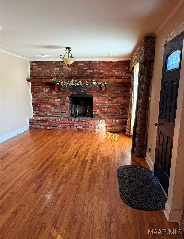 unfurnished living room with baseboards, brick wall, wood finished floors, crown molding, and a fireplace