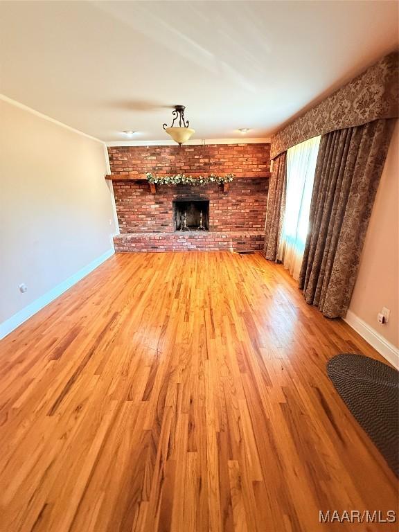 unfurnished living room featuring a brick fireplace, baseboards, and wood finished floors