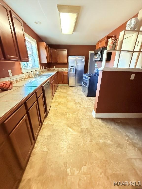 kitchen with stainless steel appliances, a sink, tile counters, and brown cabinets