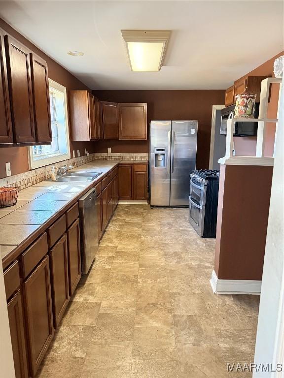 kitchen with appliances with stainless steel finishes, a sink, tile countertops, and dark brown cabinetry