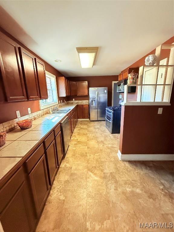 kitchen with appliances with stainless steel finishes, a sink, tile counters, and brown cabinets