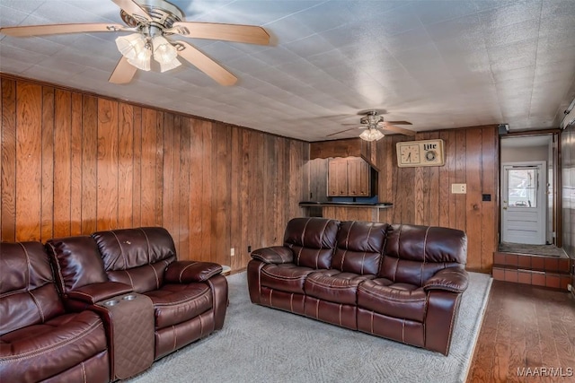 living room with ceiling fan, wooden walls, and light wood-type flooring