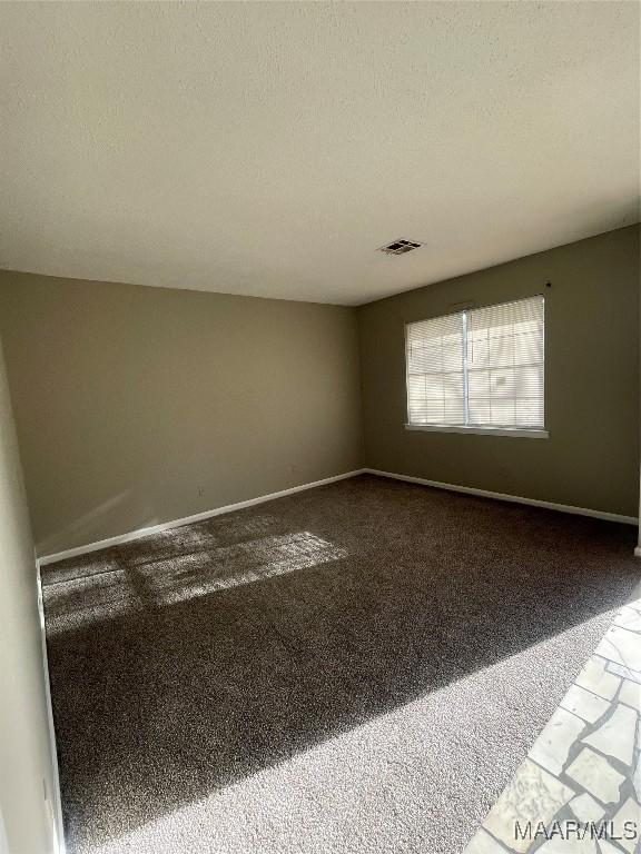 spare room with a textured ceiling, carpet floors, visible vents, and baseboards