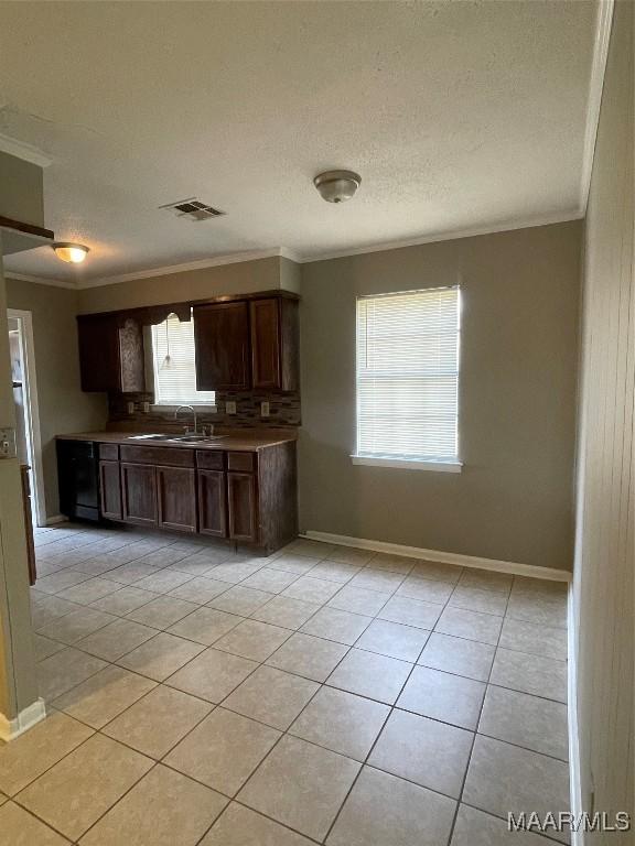 kitchen with light tile patterned floors, visible vents, ornamental molding, a sink, and dark brown cabinets