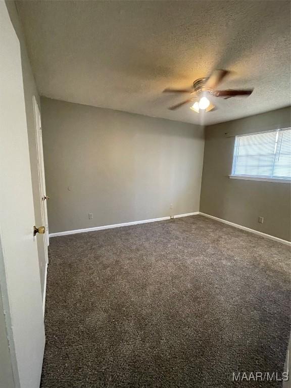 empty room featuring baseboards, dark carpet, and a textured ceiling