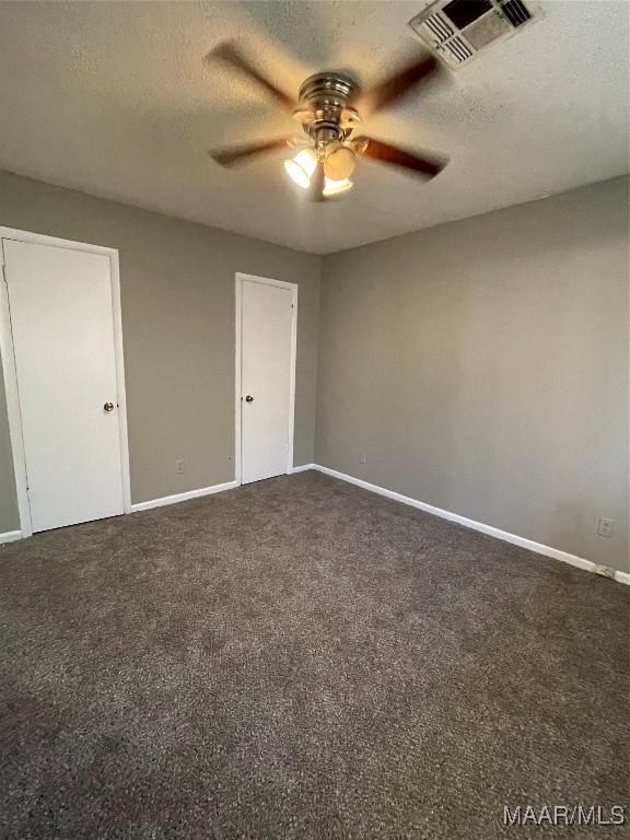 unfurnished bedroom featuring baseboards, visible vents, dark colored carpet, and a textured ceiling