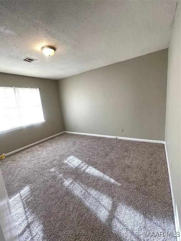 carpeted empty room with baseboards, visible vents, and a textured ceiling