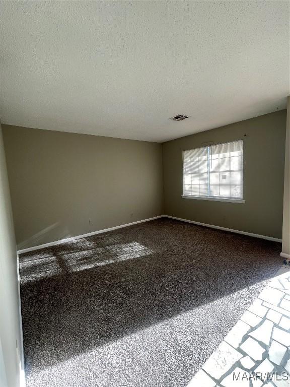 carpeted spare room featuring baseboards, visible vents, and a textured ceiling