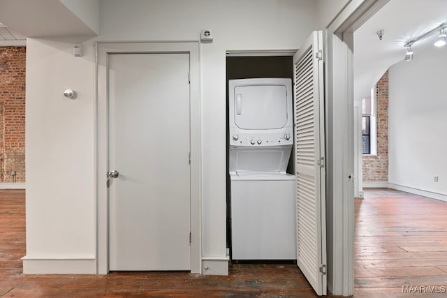 laundry area featuring dark wood-type flooring, brick wall, and stacked washer / dryer