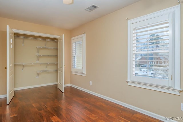 unfurnished bedroom with a closet, dark hardwood / wood-style floors, and multiple windows