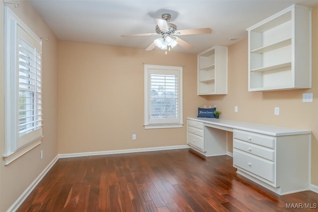 unfurnished office with dark hardwood / wood-style floors, built in desk, and ceiling fan