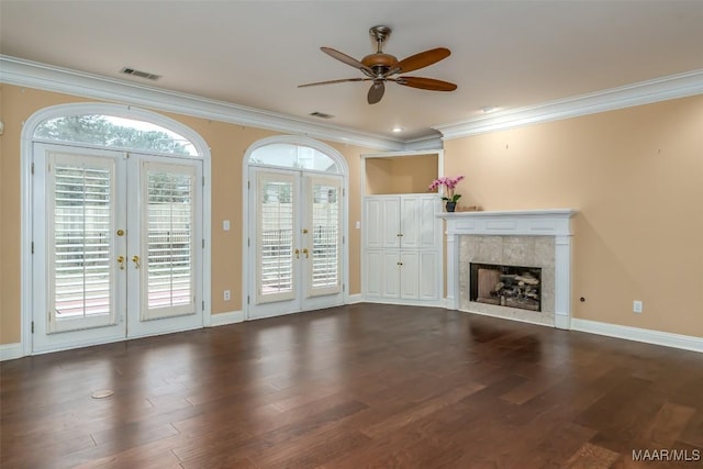 unfurnished living room featuring french doors, crown molding, dark hardwood / wood-style floors, ceiling fan, and a tiled fireplace