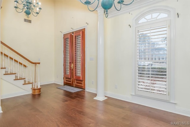 foyer entrance featuring wood-type flooring, decorative columns, french doors, and a chandelier