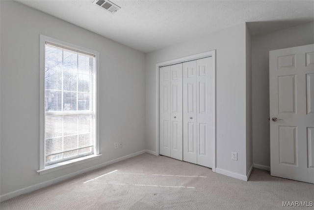 unfurnished bedroom with light carpet, multiple windows, a closet, and a textured ceiling